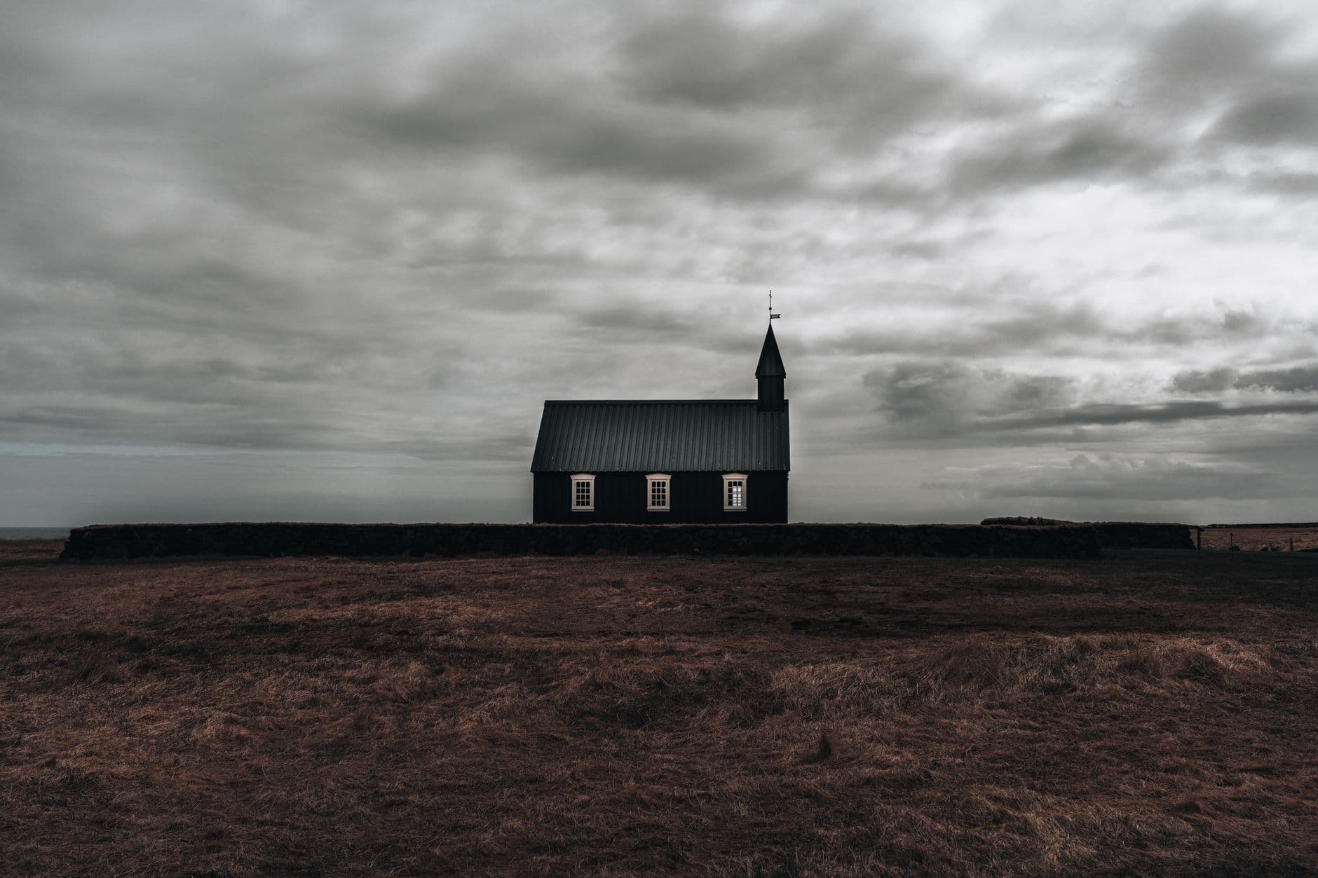 Minimalist view of a solitary church set against a moody sky, surrounded by rural fields.